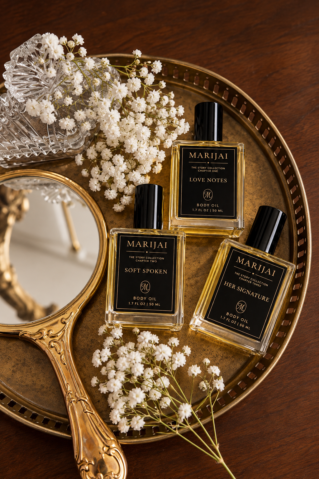 MARIJAI The Story Collection — Love Notes, Soft Spoken, and Her Signature fragrance body oils arranged on a gold tray with baby's breath and a vintage mirror
